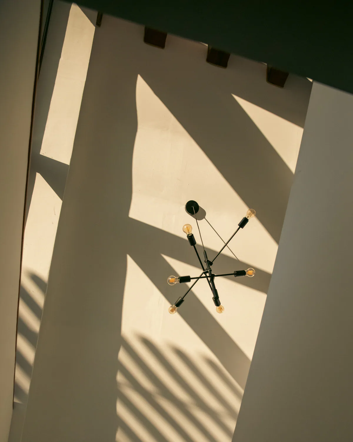 Black chandelier casting long shadows across a sunlit wall