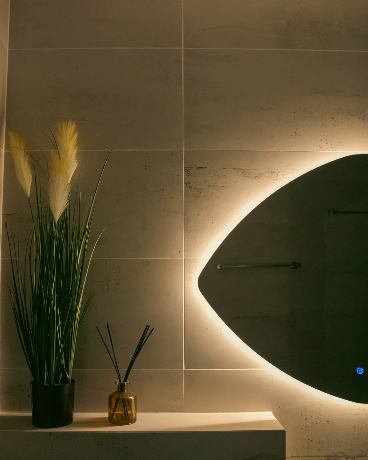 Bathroom with pampas grass, a reed diffuser, and an oval mirror edged in light