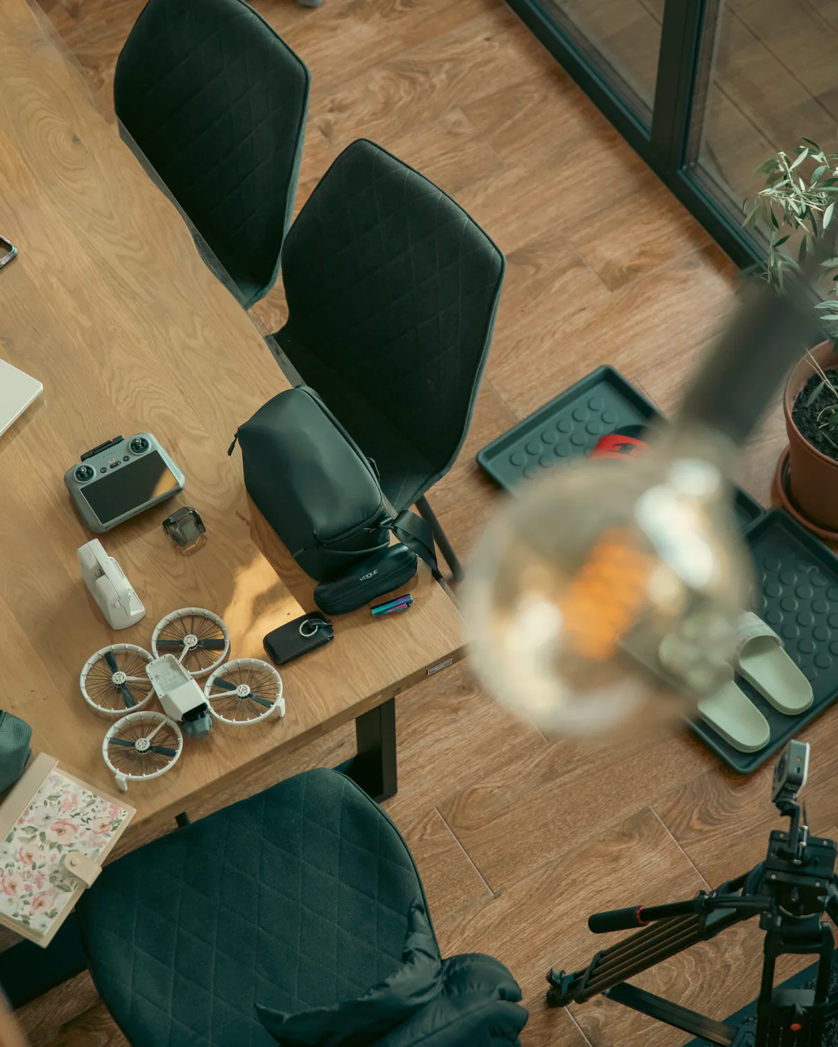 Overhead view of a wooden table with a small drone, camera, and chairs