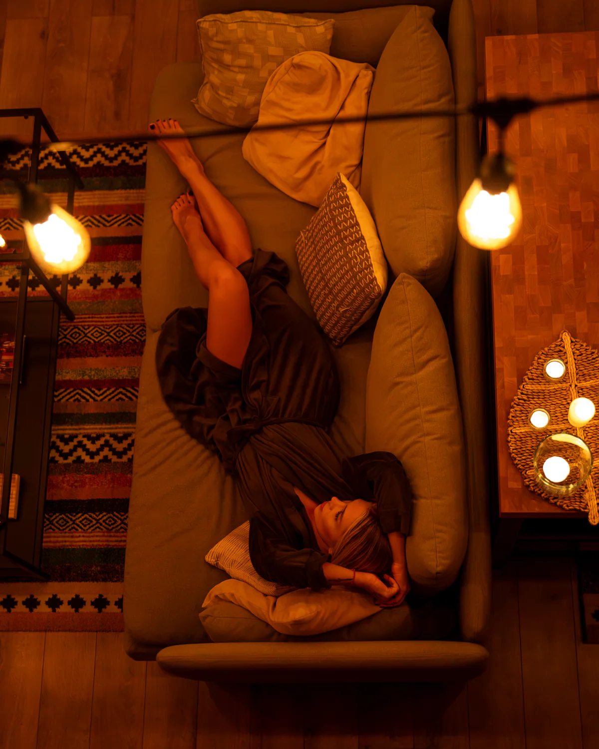 Woman relaxing on a sofa beneath warm pendant lights