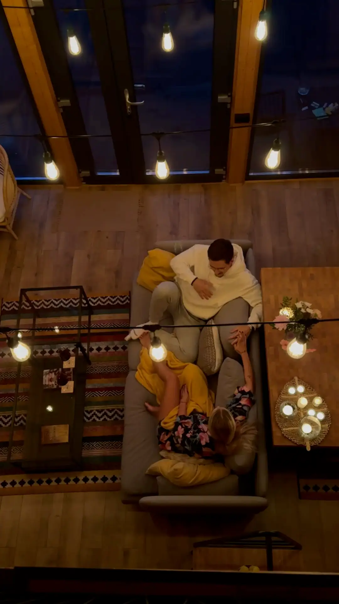 Overhead view of a couple resting together on a sofa under warm string lights