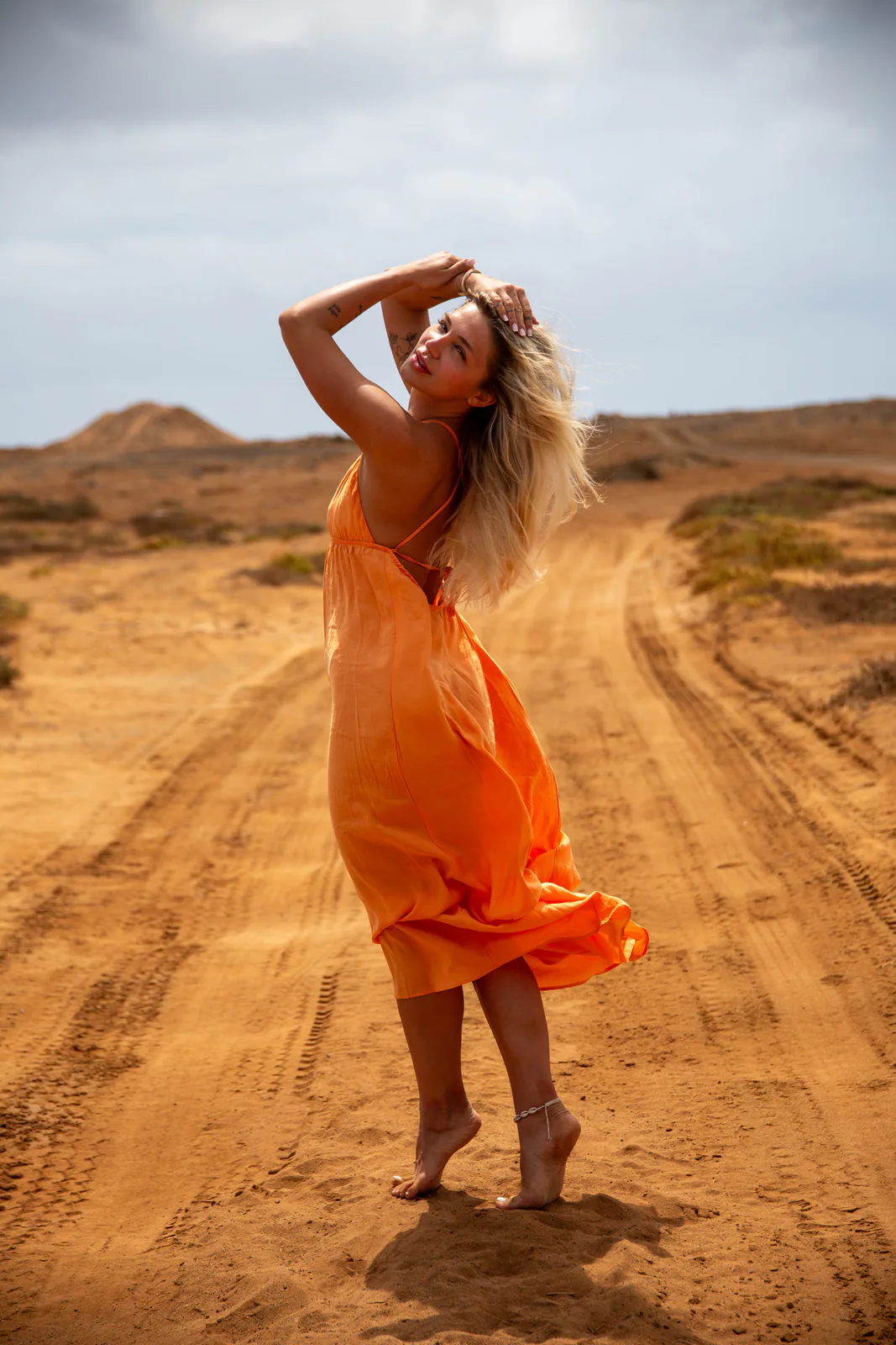 Woman in an orange dress posing in a sandy landscape