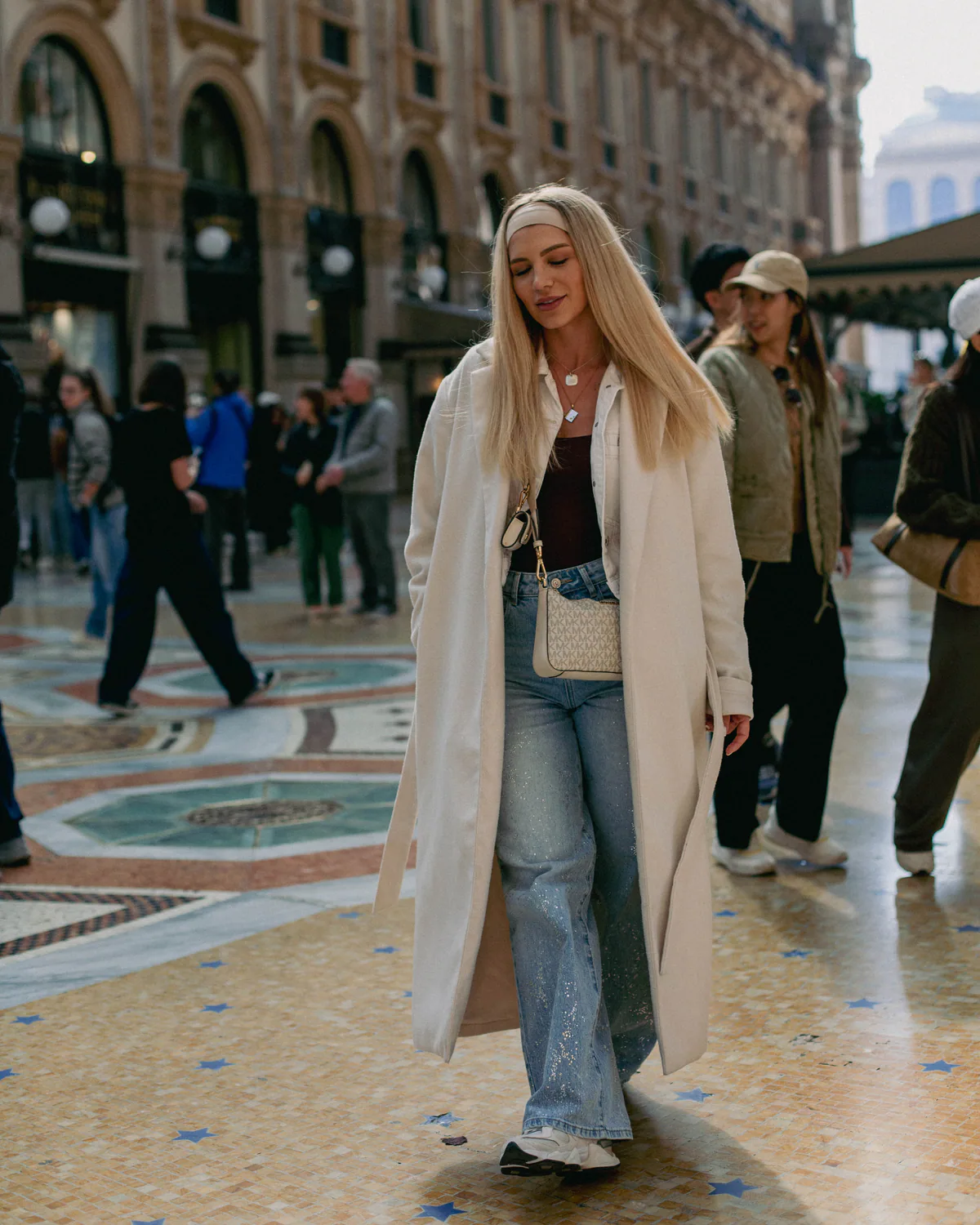Woman in a light coat walking across a patterned plaza